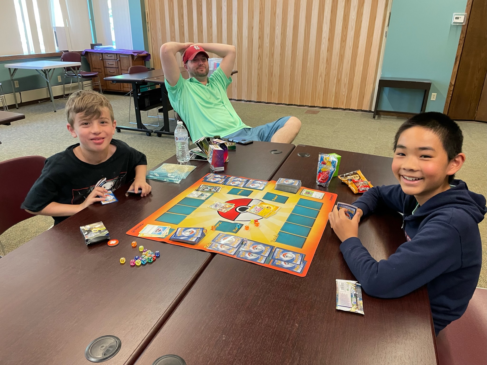 Two young boys smile at the camera in the middle of a Pokémon Trading Card Game at the Derby Neck Library.