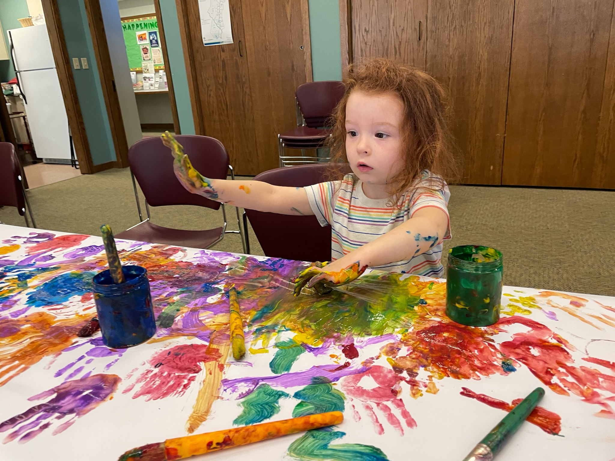 Little girl splashes in finger paint.
